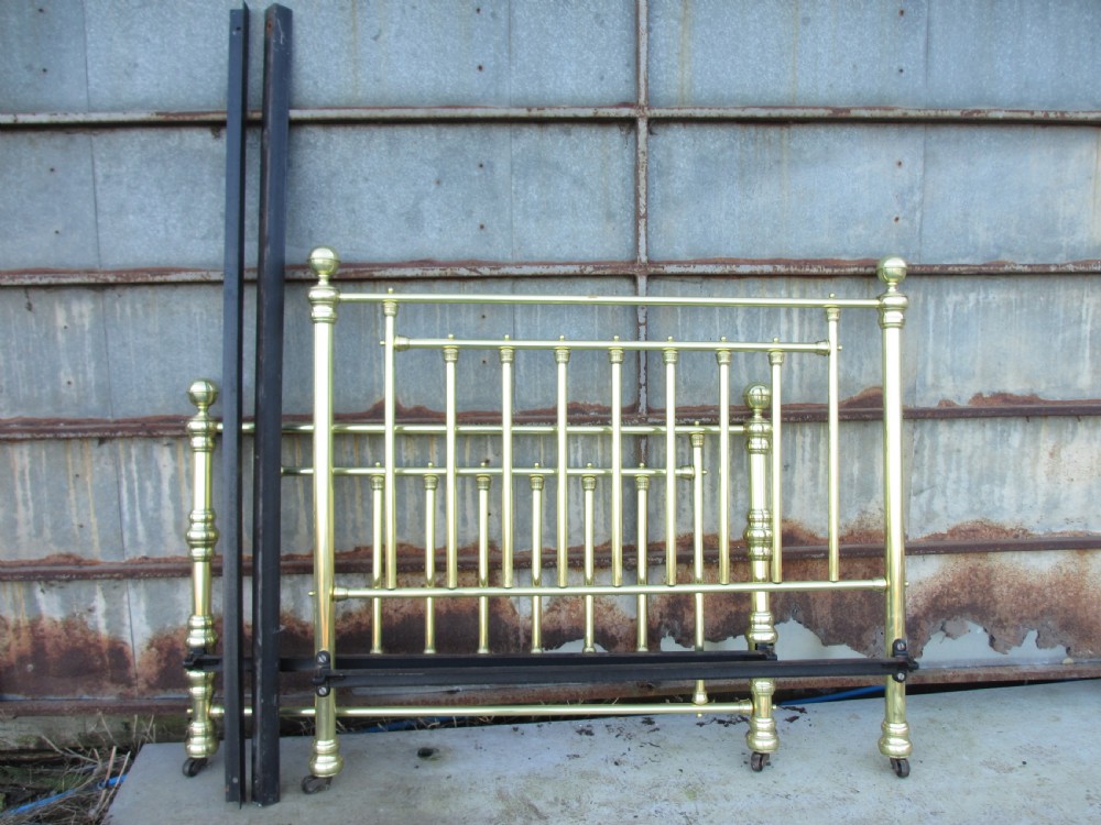 A Victorian double bedstead constructed from polished tubular brass with vertical spindles, turned posts, spherical finials, and an iron support frame on castors. View VI