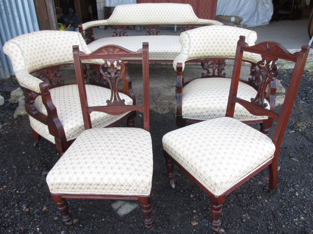 A five-piece antique mahogany parlour suite including a settee, two tub armchairs, and two side chairs with cream patterned upholstery and carved details. View X