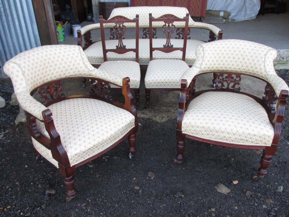 A five-piece antique mahogany parlour suite including a settee, two tub armchairs, and two side chairs with cream patterned upholstery and carved details.