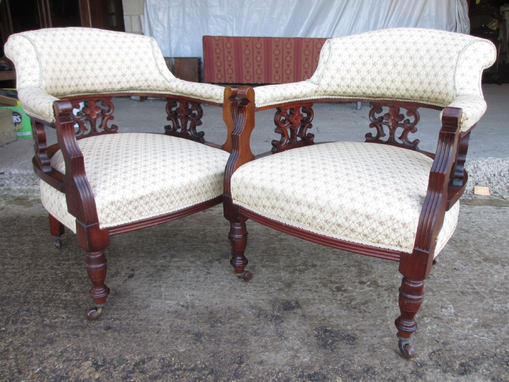A pair of antique mahogany tub armchairs featuring cream patterned fabric upholstery, openwork carved back splats, and turned front legs on castors. View II