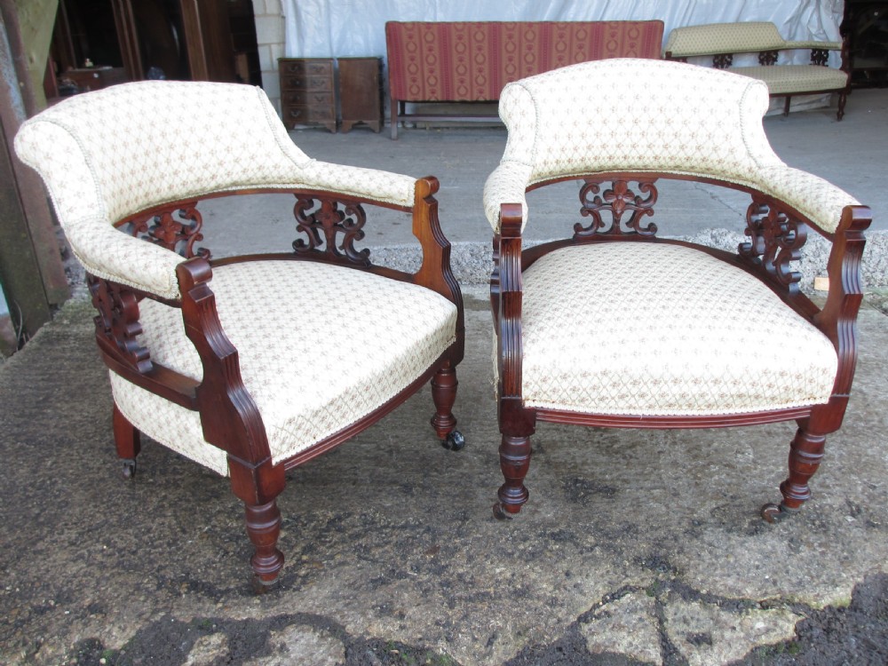 A pair of antique mahogany tub armchairs featuring cream patterned fabric upholstery, openwork carved back splats, and turned front legs on castors. View III