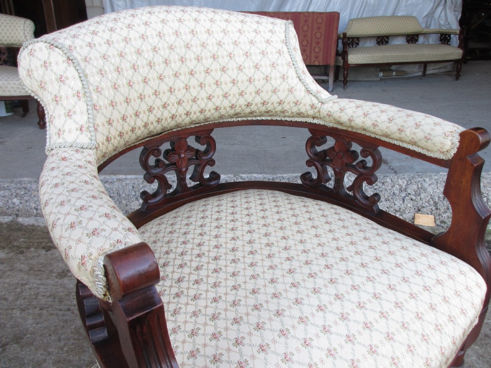 A pair of antique mahogany tub armchairs featuring cream patterned fabric upholstery, openwork carved back splats, and turned front legs on castors. View VI