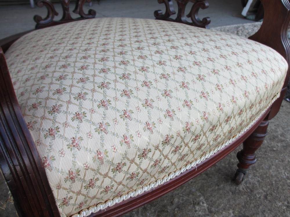 A pair of antique mahogany tub armchairs featuring cream patterned fabric upholstery, openwork carved back splats, and turned front legs on castors. View XI