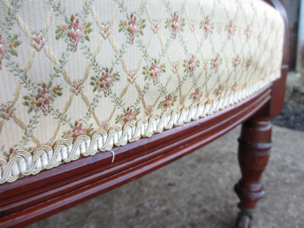 A pair of antique mahogany tub armchairs featuring cream patterned fabric upholstery, openwork carved back splats, and turned front legs on castors. View XII