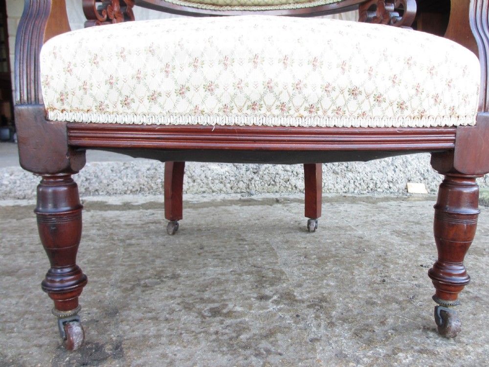 A pair of antique mahogany tub armchairs featuring cream patterned fabric upholstery, openwork carved back splats, and turned front legs on castors. View XIII