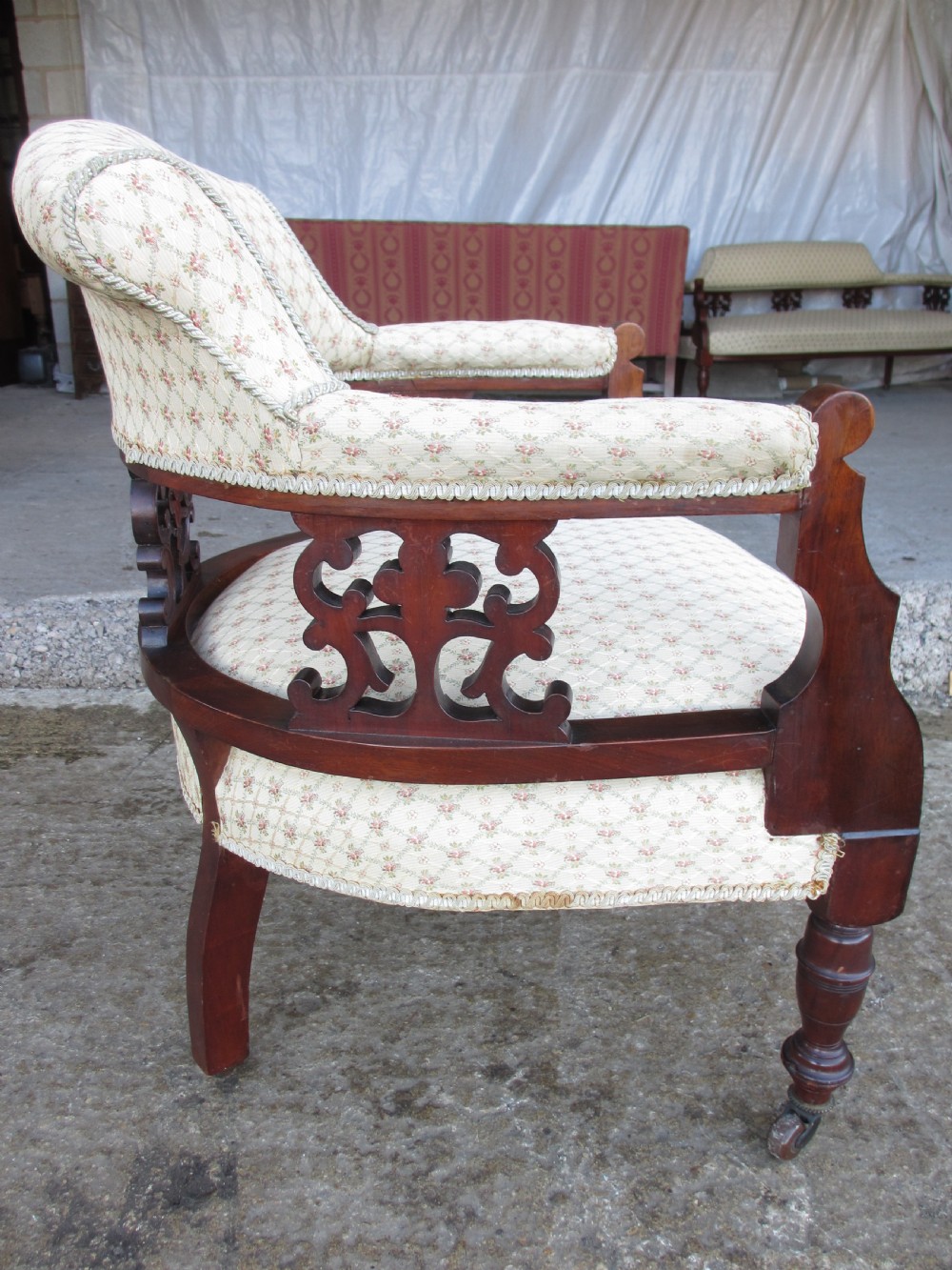 A pair of antique mahogany tub armchairs featuring cream patterned fabric upholstery, openwork carved back splats, and turned front legs on castors. View XV