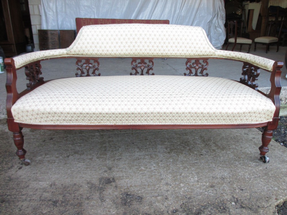 An Edwardian mahogany settee featuring a padded backrest and seat upholstered in cream patterned fabric, supported by carved back splats and turned front legs on castors.