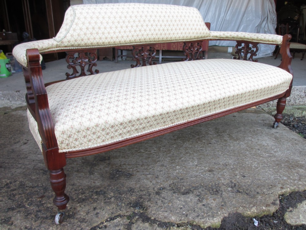 An Edwardian mahogany settee featuring a padded backrest and seat upholstered in cream patterned fabric, supported by carved back splats and turned front legs on castors. View II