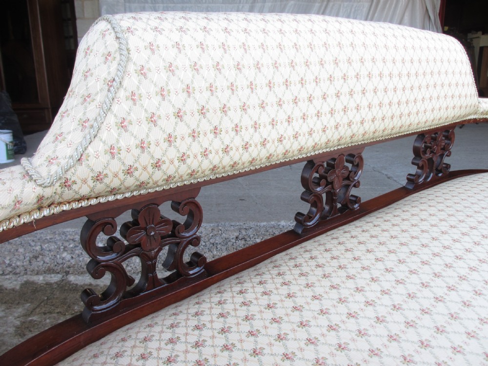 An Edwardian mahogany settee featuring a padded backrest and seat upholstered in cream patterned fabric, supported by carved back splats and turned front legs on castors. View III