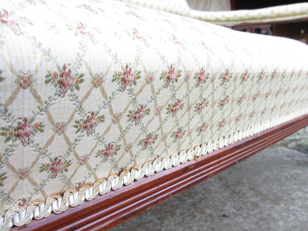An Edwardian mahogany settee featuring a padded backrest and seat upholstered in cream patterned fabric, supported by carved back splats and turned front legs on castors. View VII