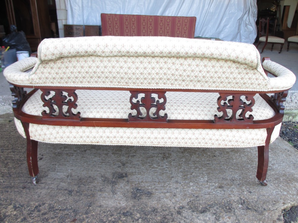An Edwardian mahogany settee featuring a padded backrest and seat upholstered in cream patterned fabric, supported by carved back splats and turned front legs on castors. View XI