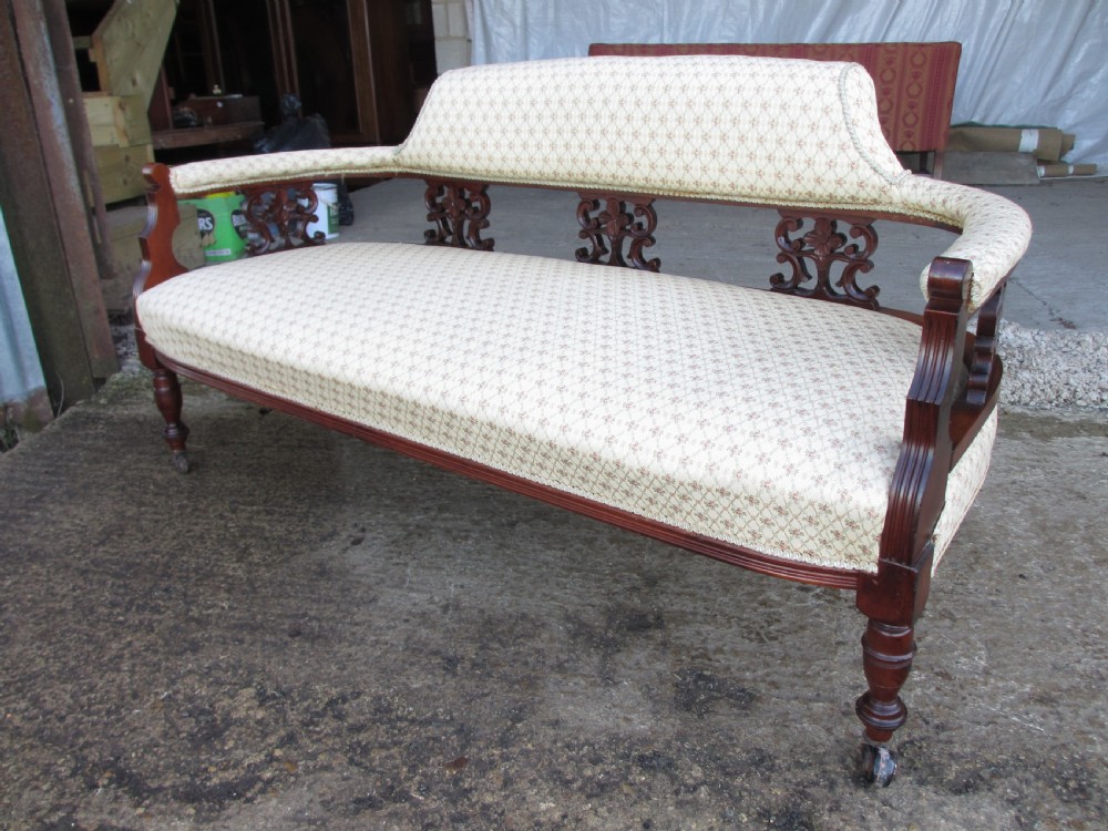 An Edwardian mahogany settee featuring a padded backrest and seat upholstered in cream patterned fabric, supported by carved back splats and turned front legs on castors. View XII