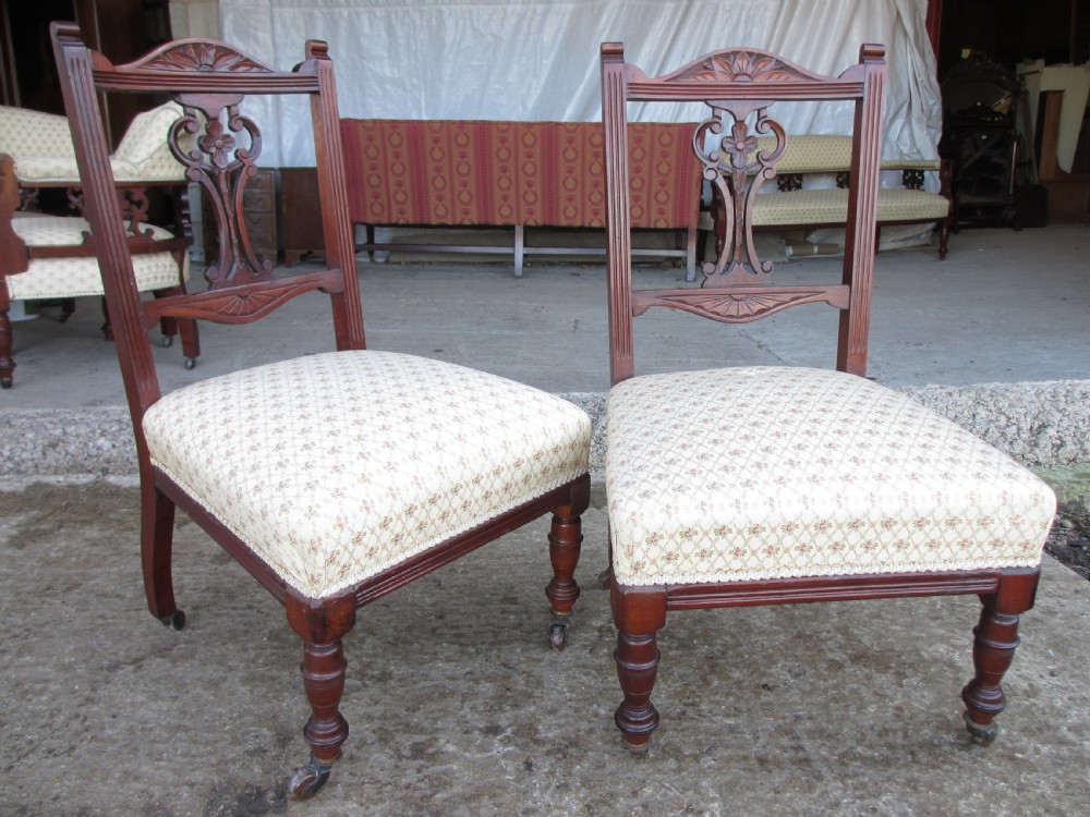 A pair of Edwardian mahogany nursing chairs featuring low seats, pattern-upholstered cushions, carved backs with decorative central splats, and turned front legs with castors. View II