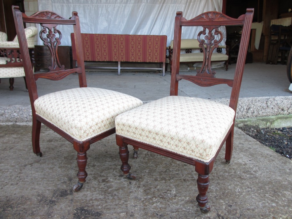 A pair of Edwardian mahogany nursing chairs featuring low seats, pattern-upholstered cushions, carved backs with decorative central splats, and turned front legs with castors. View III