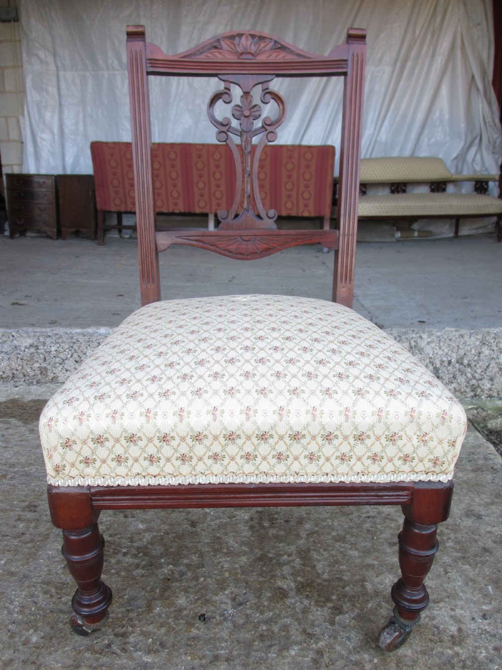 A pair of Edwardian mahogany nursing chairs featuring low seats, pattern-upholstered cushions, carved backs with decorative central splats, and turned front legs with castors. View IV