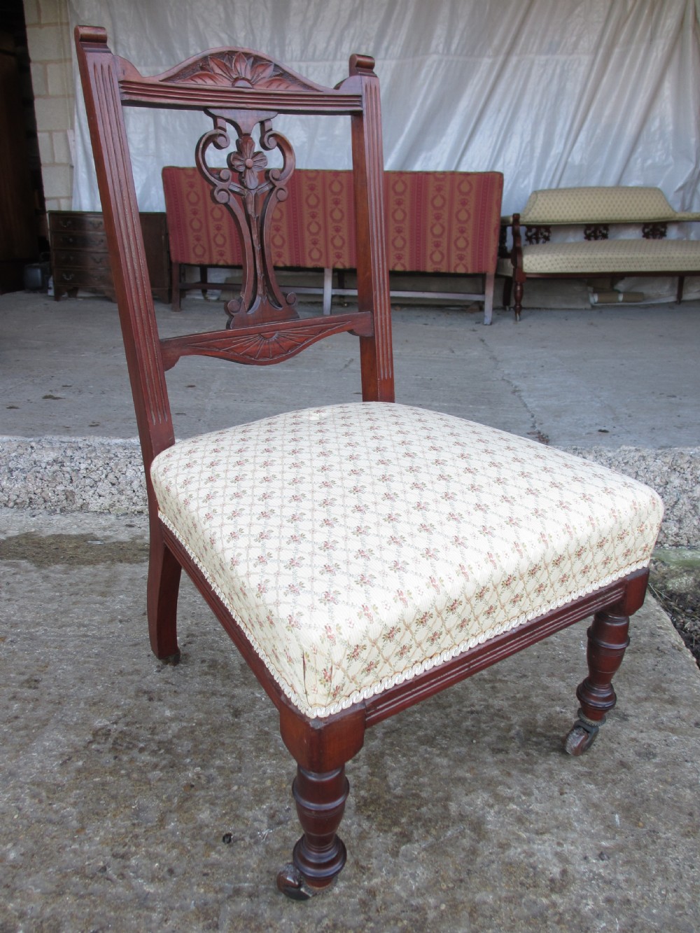 A pair of Edwardian mahogany nursing chairs featuring low seats, pattern-upholstered cushions, carved backs with decorative central splats, and turned front legs with castors. View V