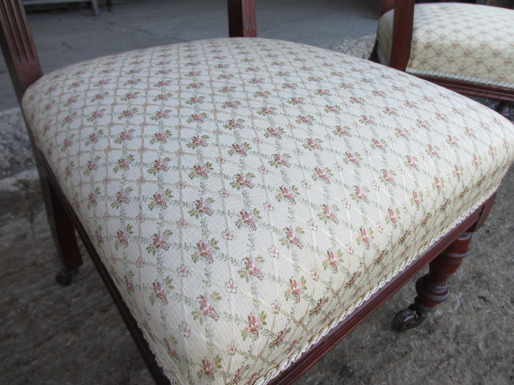 A pair of Edwardian mahogany nursing chairs featuring low seats, pattern-upholstered cushions, carved backs with decorative central splats, and turned front legs with castors. View IX