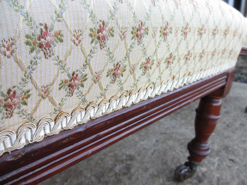 A pair of Edwardian mahogany nursing chairs featuring low seats, pattern-upholstered cushions, carved backs with decorative central splats, and turned front legs with castors. View X
