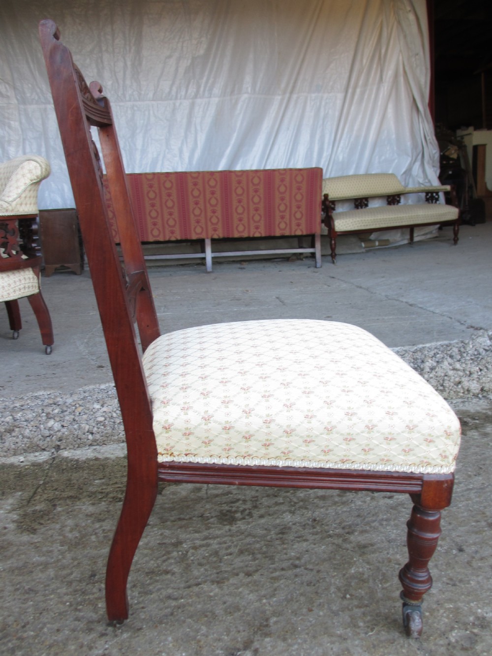 A pair of Edwardian mahogany nursing chairs featuring low seats, pattern-upholstered cushions, carved backs with decorative central splats, and turned front legs with castors. View XIII