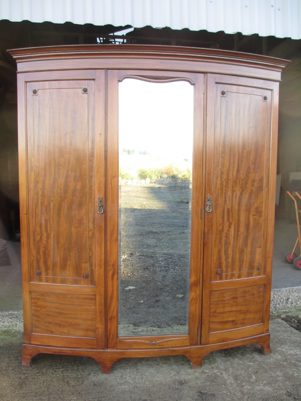 A Victorian bow-fronted mahogany triple wardrobe featuring a central full-length mirror door flanked by panelled flame mahogany doors.