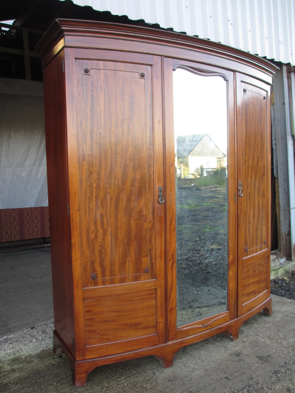 A Victorian bow-fronted mahogany triple wardrobe featuring a central full-length mirror door flanked by panelled flame mahogany doors. View III