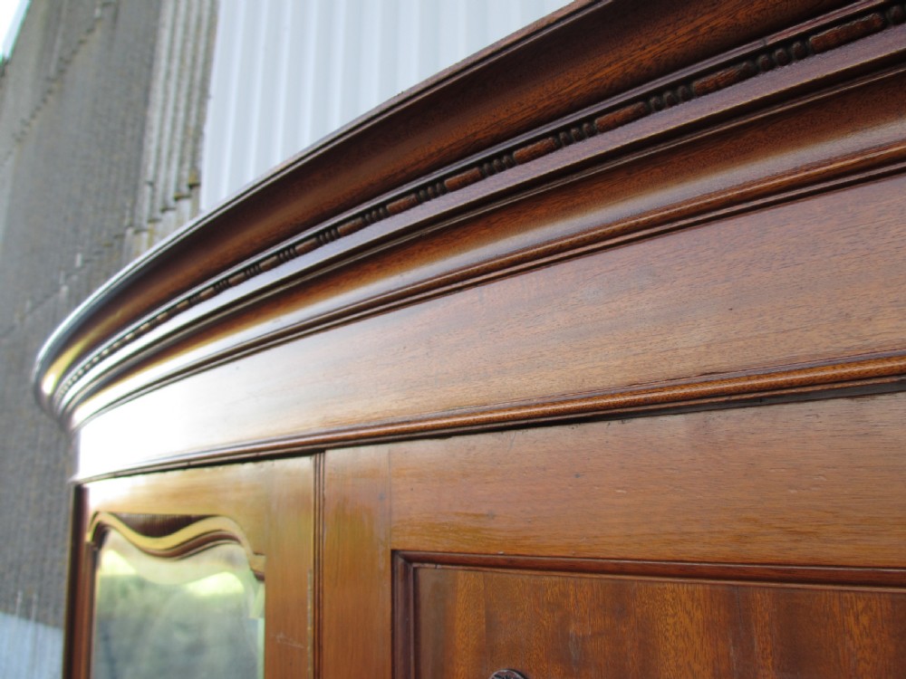 A Victorian bow-fronted mahogany triple wardrobe featuring a central full-length mirror door flanked by panelled flame mahogany doors. View V
