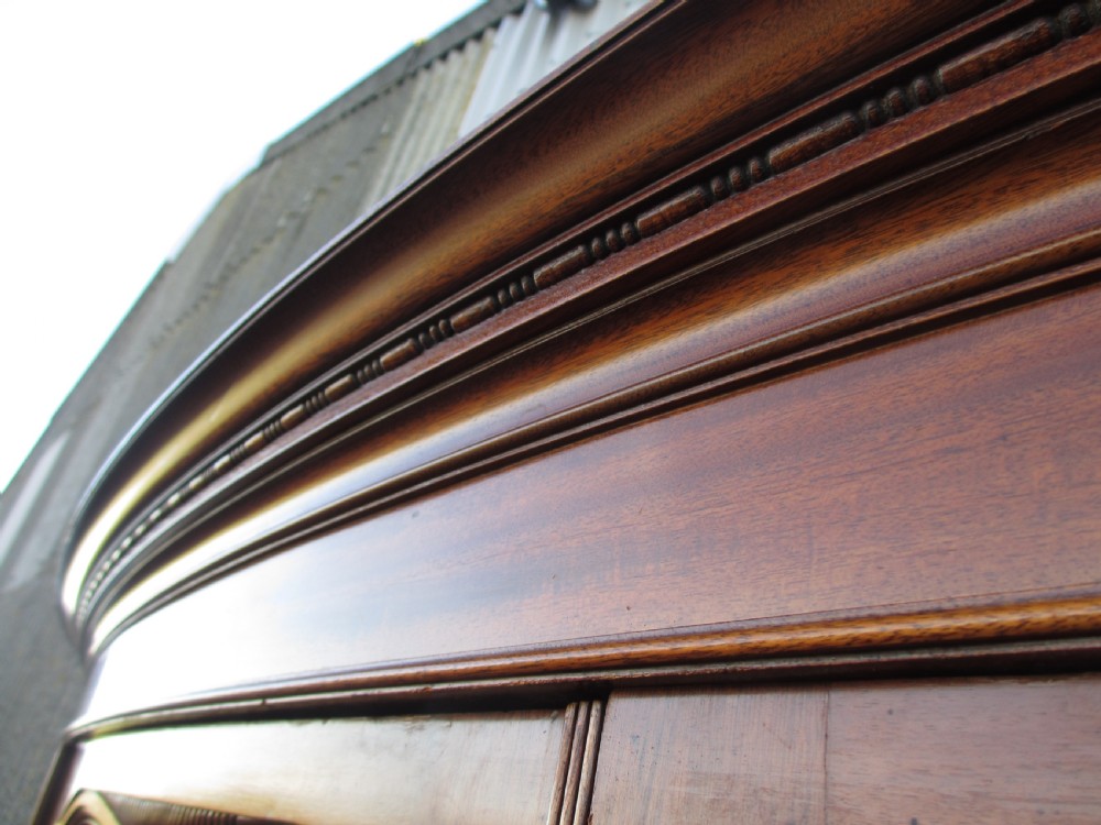 A Victorian bow-fronted mahogany triple wardrobe featuring a central full-length mirror door flanked by panelled flame mahogany doors. View VI