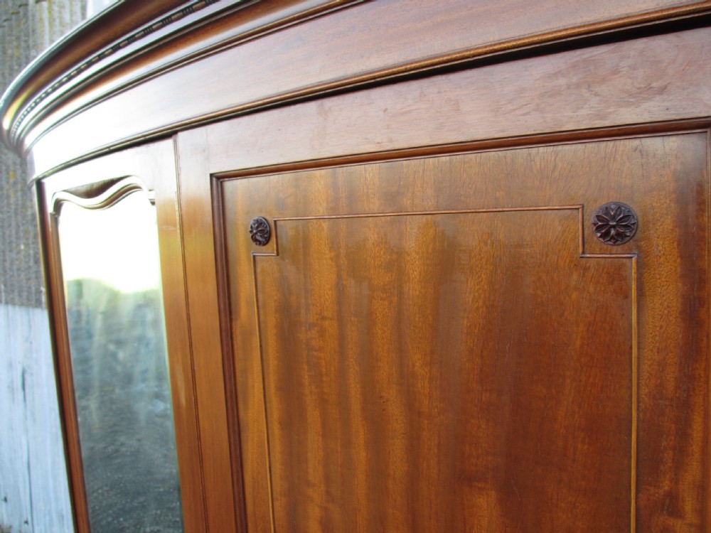 A Victorian bow-fronted mahogany triple wardrobe featuring a central full-length mirror door flanked by panelled flame mahogany doors. View VII