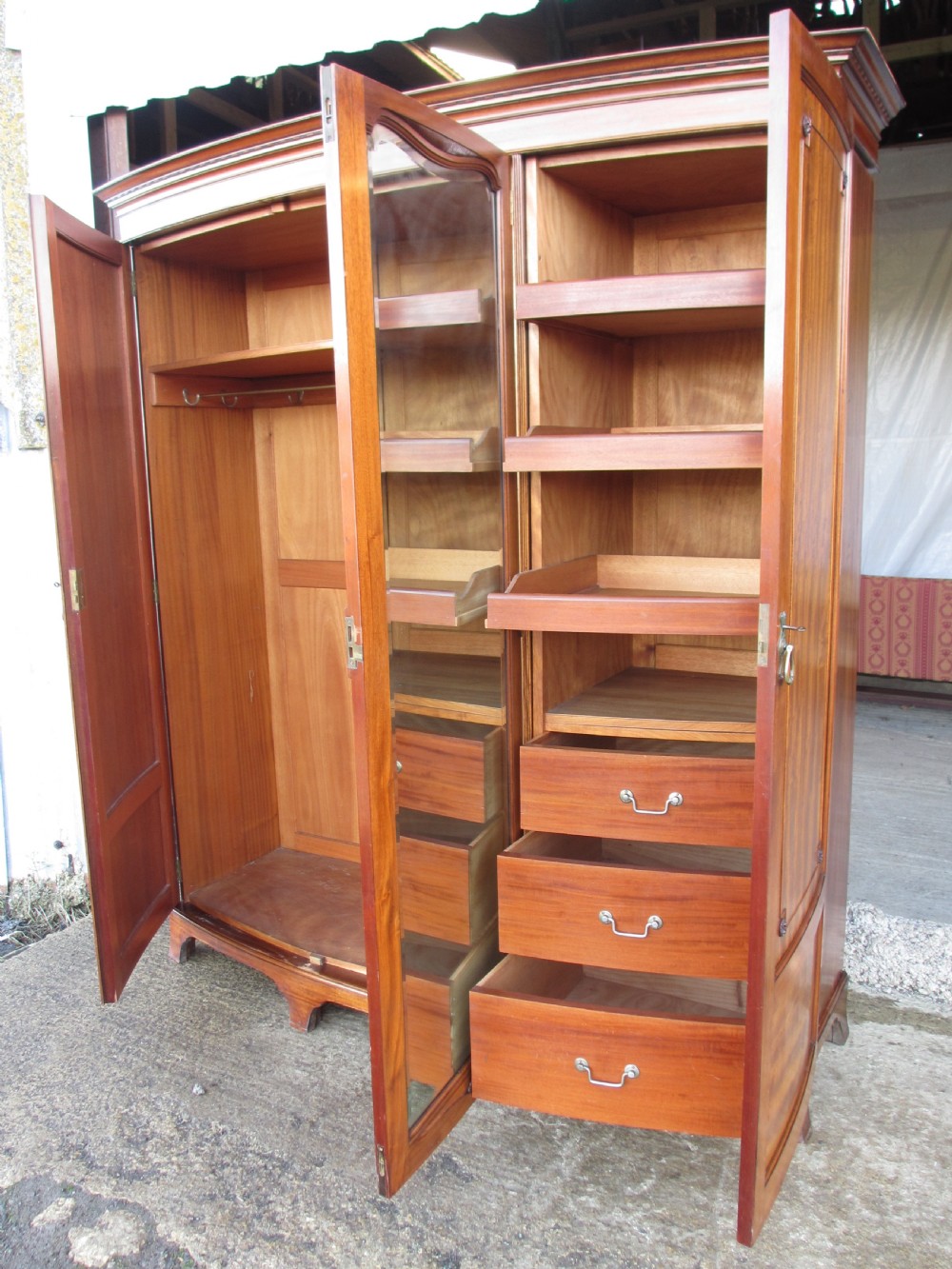 A Victorian bow-fronted mahogany triple wardrobe featuring a central full-length mirror door flanked by panelled flame mahogany doors. View XV
