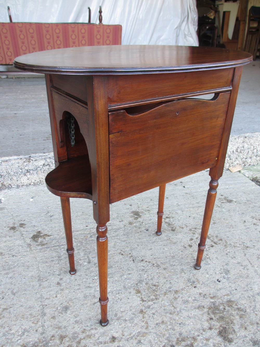 Victorian mahogany oval occasional table with lower shelf and fold-down side leaves held by metal chains. View II