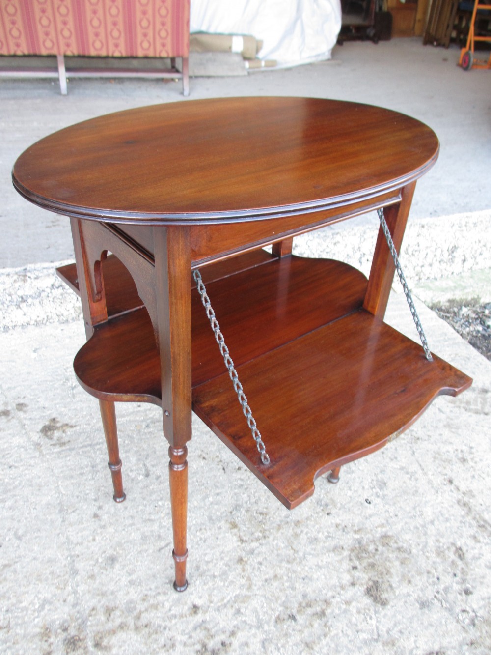 Victorian mahogany oval occasional table with lower shelf and fold-down side leaves held by metal chains.