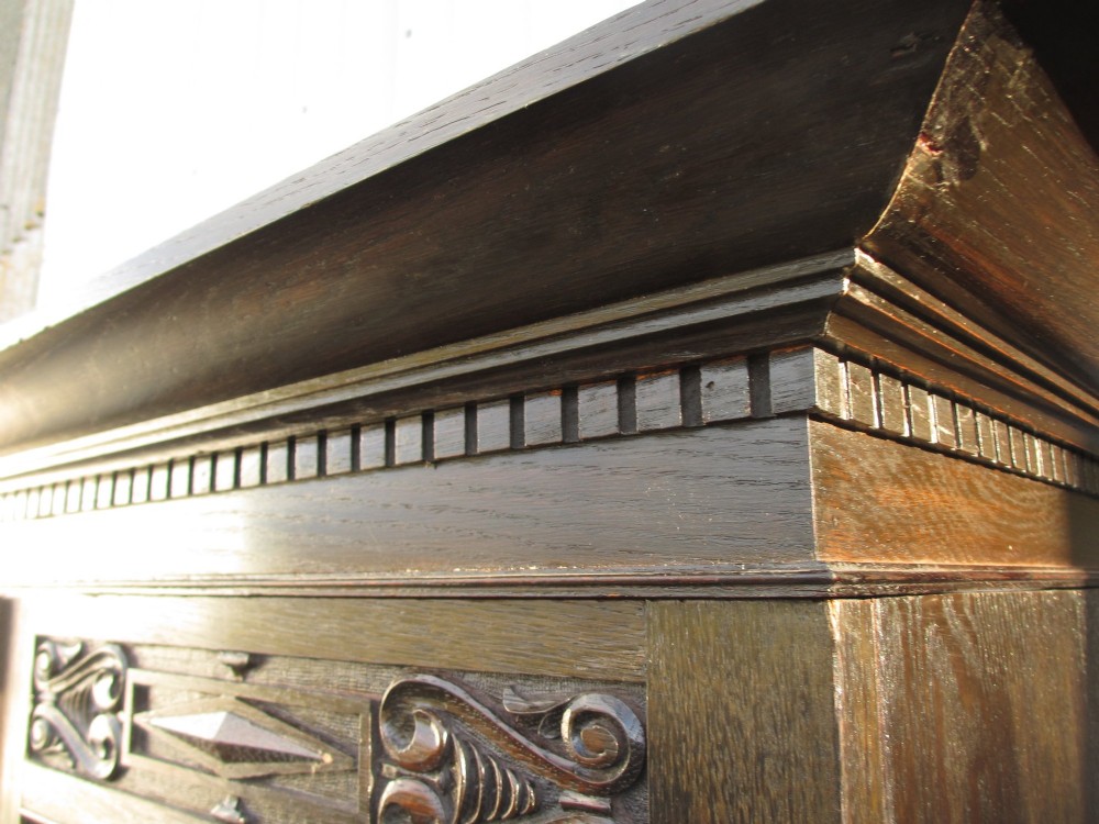 An Edwardian dark oak triple wardrobe featuring carved decorative panels on the side doors, an arched mirrored centre door, and flattened bun feet. View IV