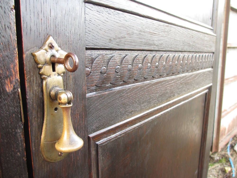 An Edwardian dark oak triple wardrobe featuring carved decorative panels on the side doors, an arched mirrored centre door, and flattened bun feet. View VI