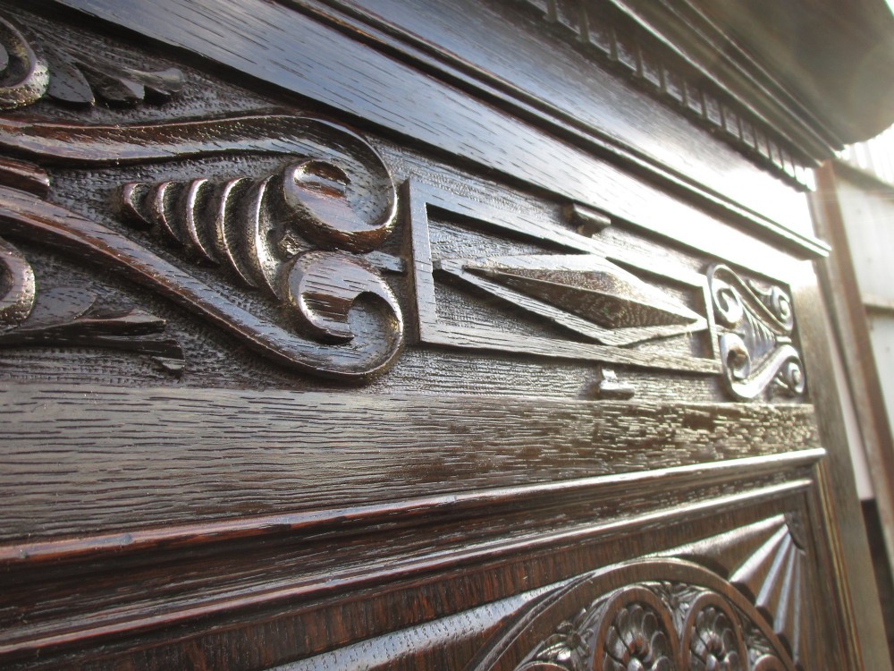 An Edwardian dark oak triple wardrobe featuring carved decorative panels on the side doors, an arched mirrored centre door, and flattened bun feet. View IX