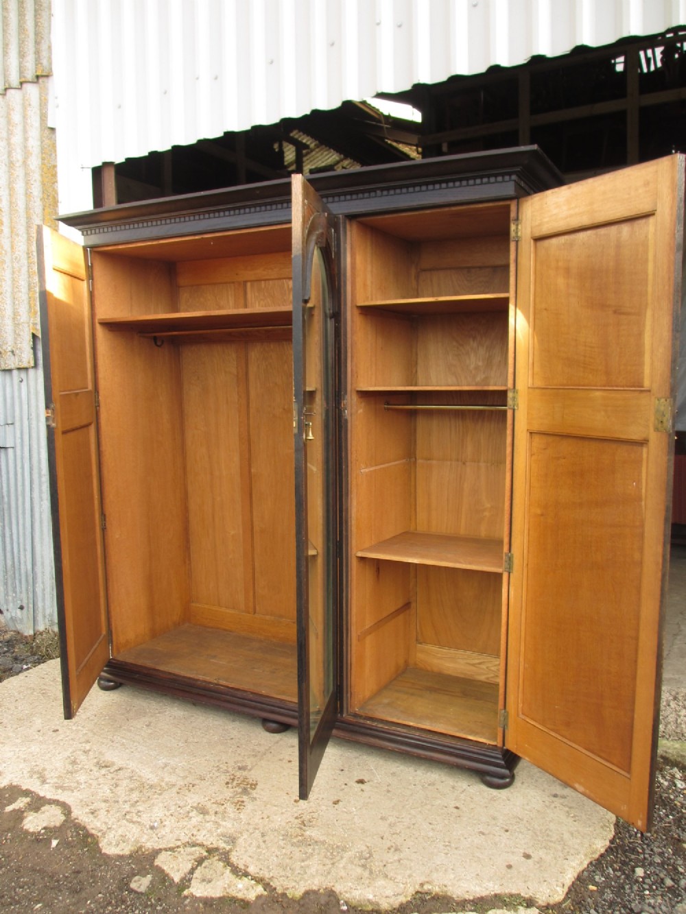 An Edwardian dark oak triple wardrobe featuring carved decorative panels on the side doors, an arched mirrored centre door, and flattened bun feet. View XI