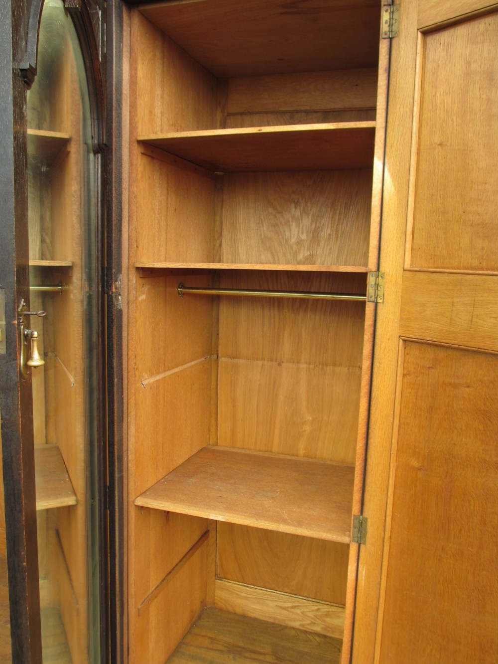An Edwardian dark oak triple wardrobe featuring carved decorative panels on the side doors, an arched mirrored centre door, and flattened bun feet. View XII