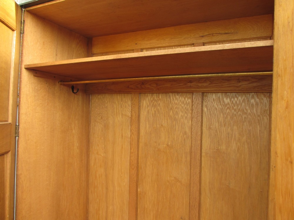 An Edwardian dark oak triple wardrobe featuring carved decorative panels on the side doors, an arched mirrored centre door, and flattened bun feet. View XIII
