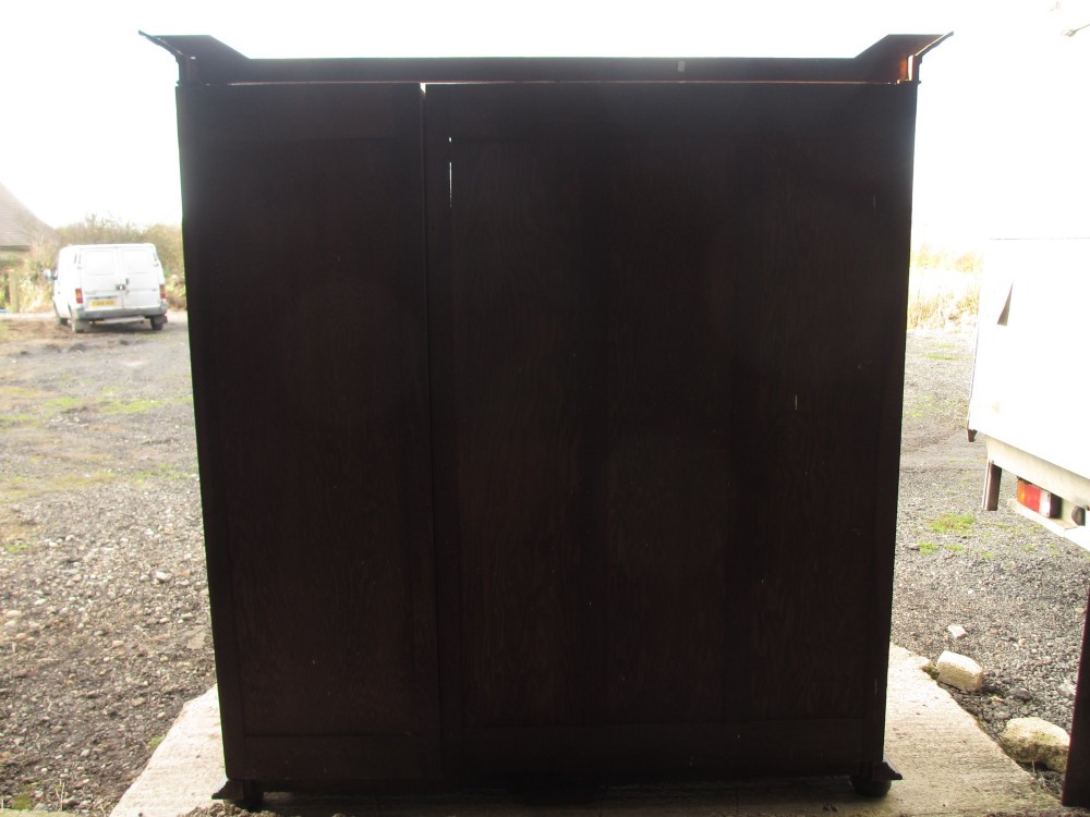 An Edwardian dark oak triple wardrobe featuring carved decorative panels on the side doors, an arched mirrored centre door, and flattened bun feet. View XV