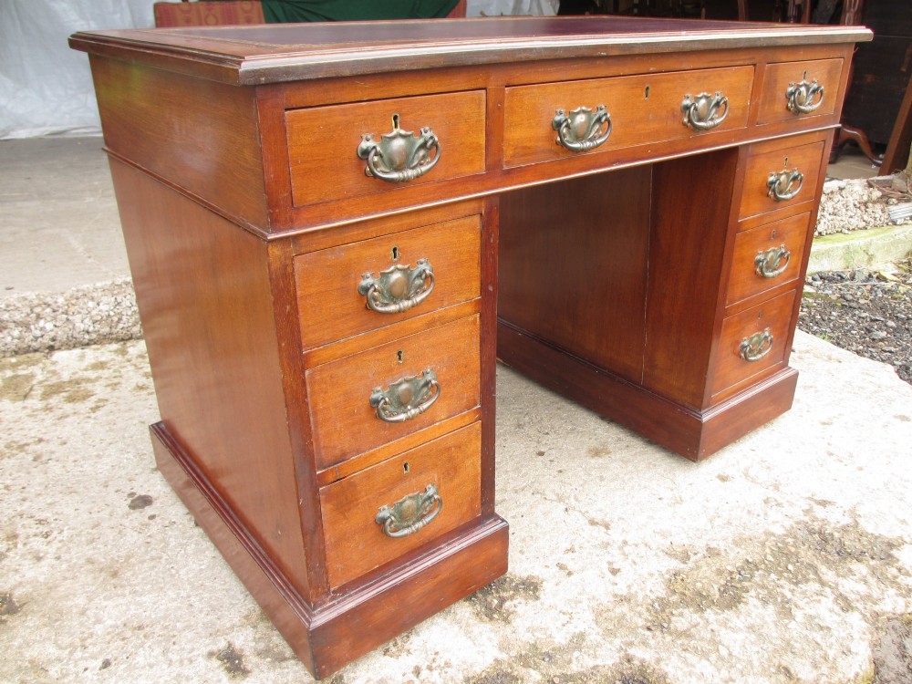 A Victorian walnut pedestal desk featuring nine drawers with brass drop handles and a maroon tooled leather inset writing surface. View II