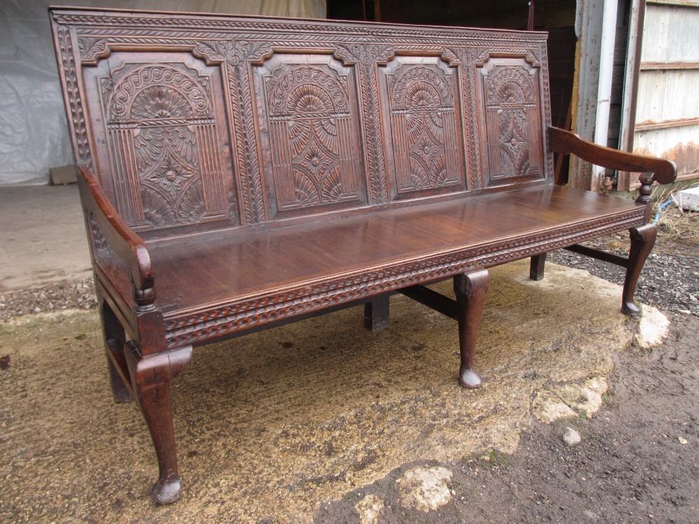 An 18th-century dark oak hall settle featuring four carved arch back panels, curved armrests, and cabriole front legs. View II