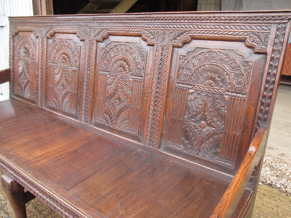 An 18th-century dark oak hall settle featuring four carved arch back panels, curved armrests, and cabriole front legs. View III