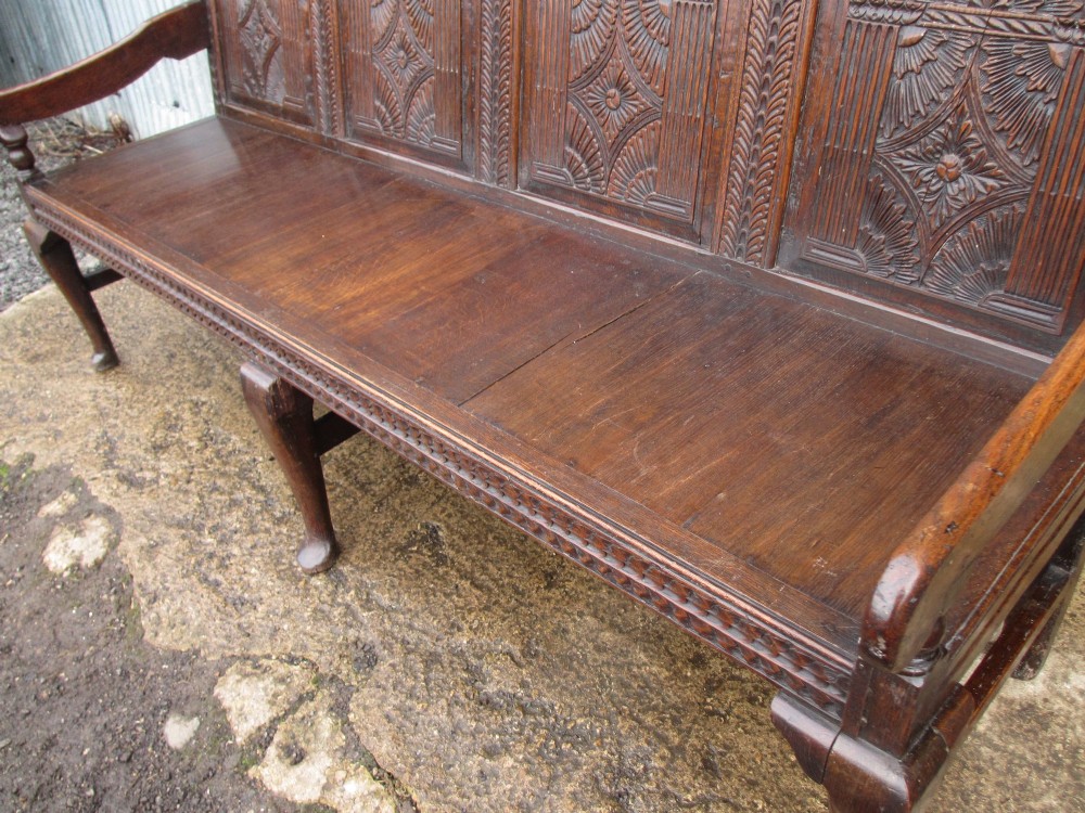 An 18th-century dark oak hall settle featuring four carved arch back panels, curved armrests, and cabriole front legs. View IV