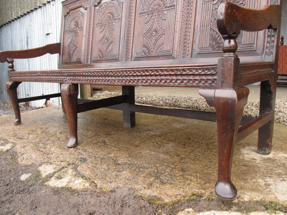 An 18th-century dark oak hall settle featuring four carved arch back panels, curved armrests, and cabriole front legs. View V
