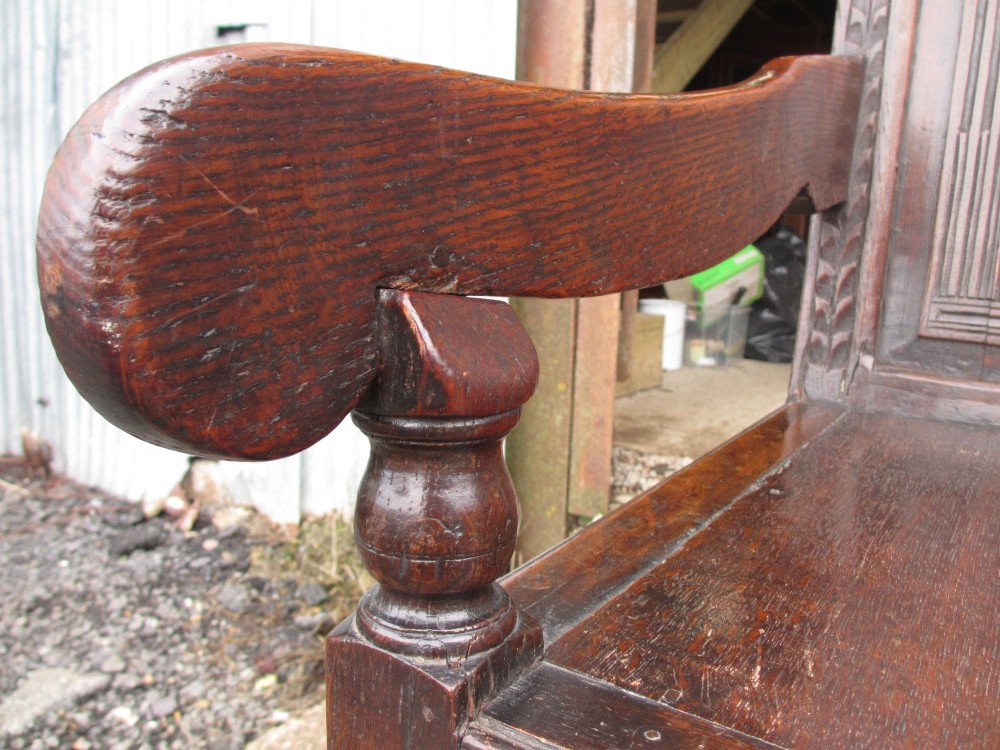 An 18th-century dark oak hall settle featuring four carved arch back panels, curved armrests, and cabriole front legs. View VI