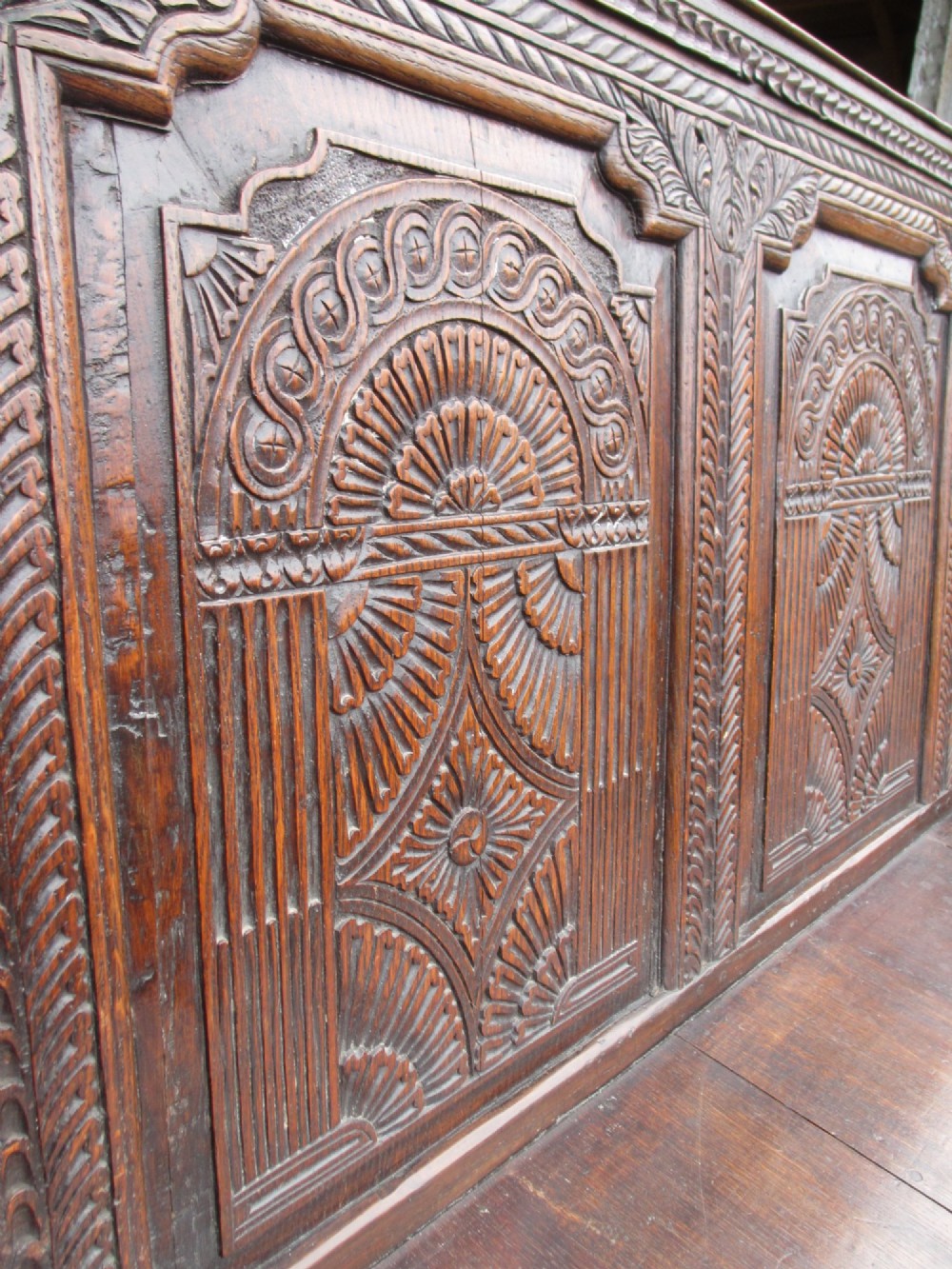 An 18th-century dark oak hall settle featuring four carved arch back panels, curved armrests, and cabriole front legs. View IX
