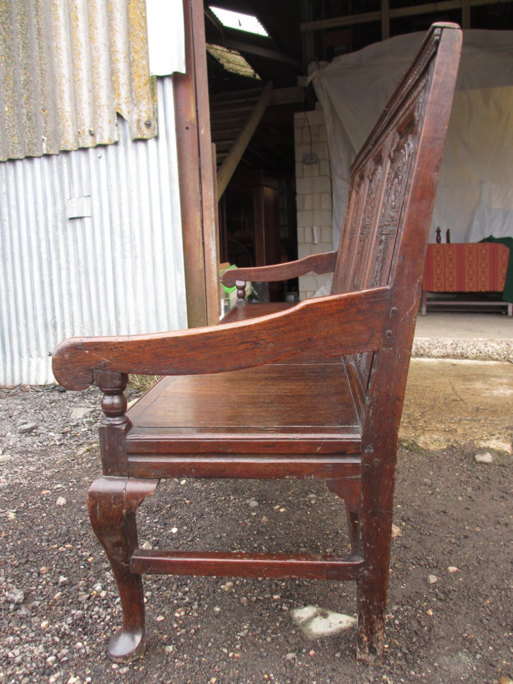 An 18th-century dark oak hall settle featuring four carved arch back panels, curved armrests, and cabriole front legs. View XIII