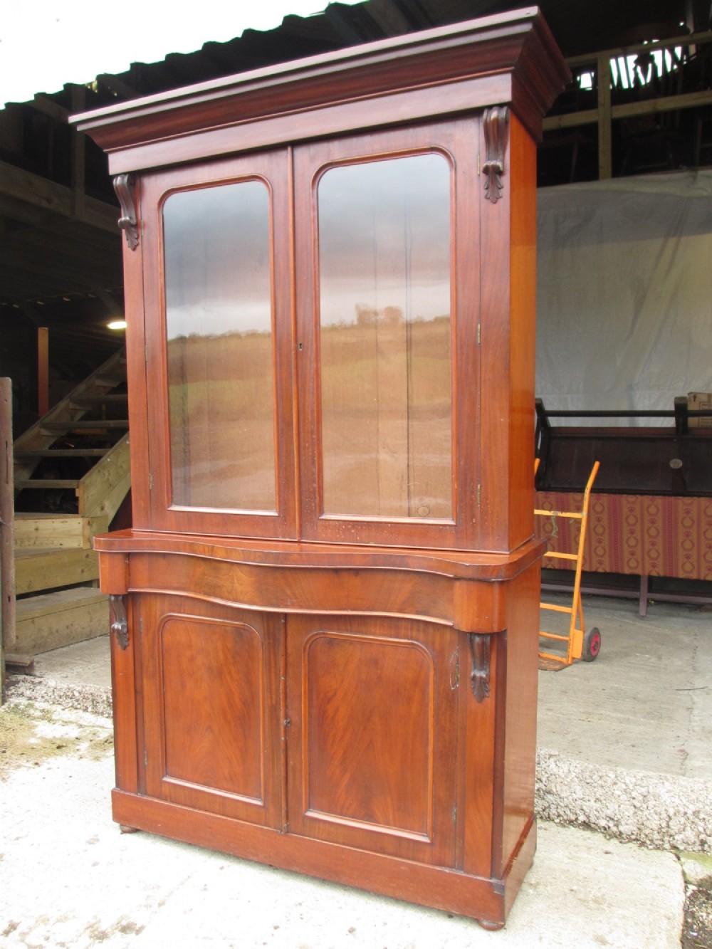 A two-piece Victorian mahogany bookcase featuring an upper section with two glazed doors and carved corbels over a lower cabinet with flame mahogany panelled doors. View II