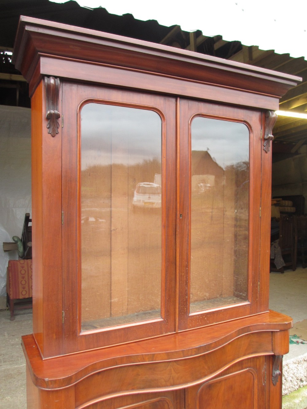 A two-piece Victorian mahogany bookcase featuring an upper section with two glazed doors and carved corbels over a lower cabinet with flame mahogany panelled doors. View III
