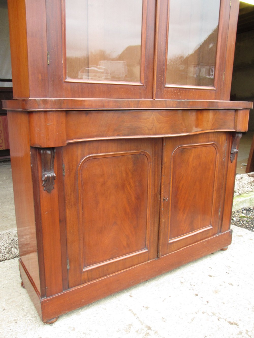 A two-piece Victorian mahogany bookcase featuring an upper section with two glazed doors and carved corbels over a lower cabinet with flame mahogany panelled doors. View IV