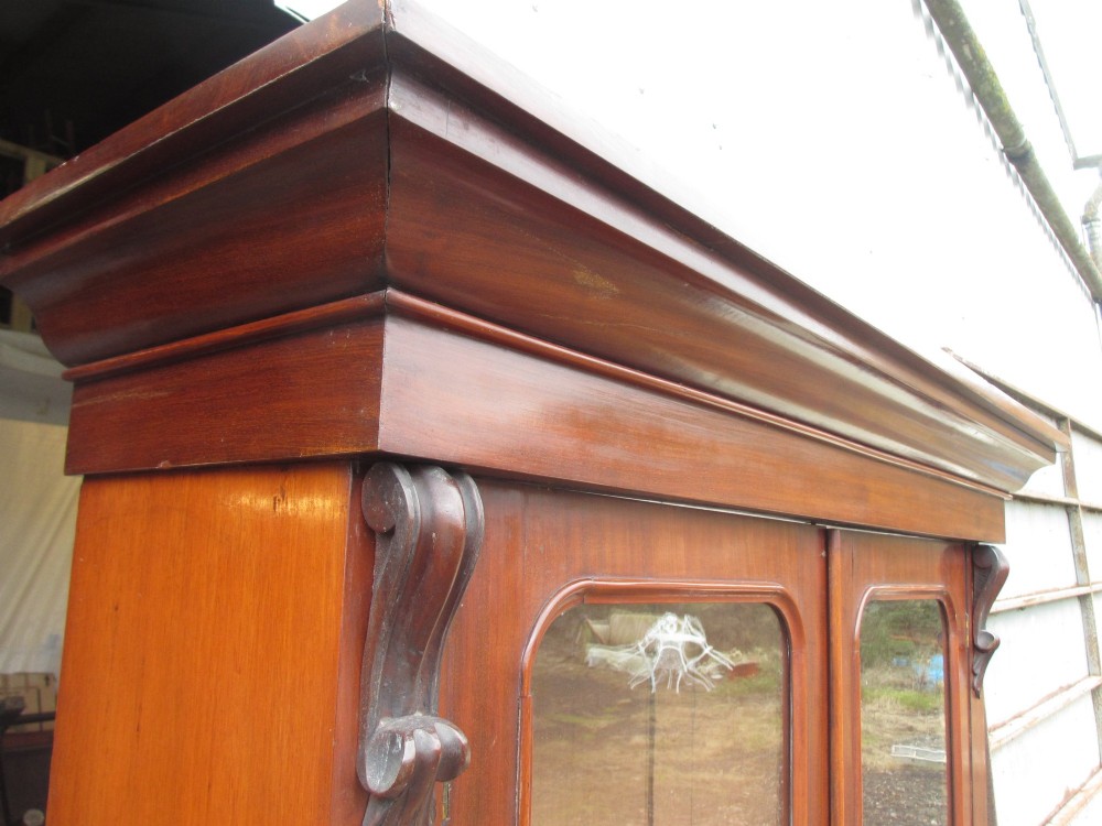 A two-piece Victorian mahogany bookcase featuring an upper section with two glazed doors and carved corbels over a lower cabinet with flame mahogany panelled doors. View V